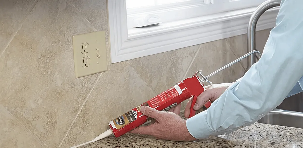 Handyman applying caulk along a kitchen backsplash and countertop seam in Orlando, FL